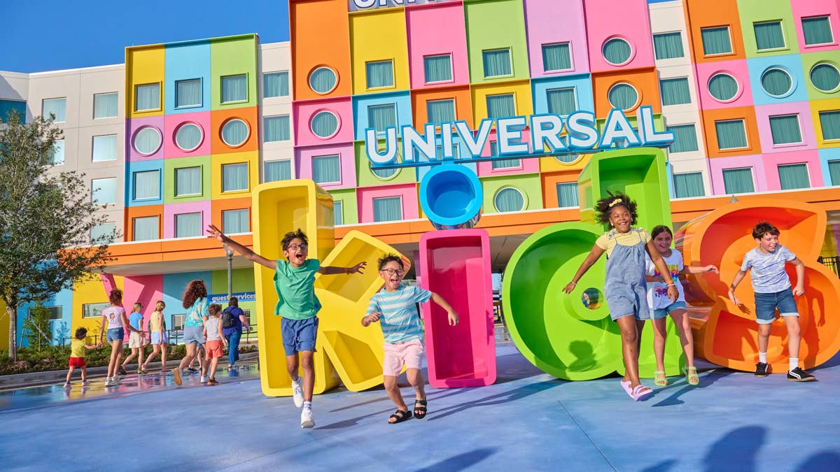 Kids jumping for joy in front of the giant Universal Kids Resort entrance sign and its colorful resort hotel in Frisco