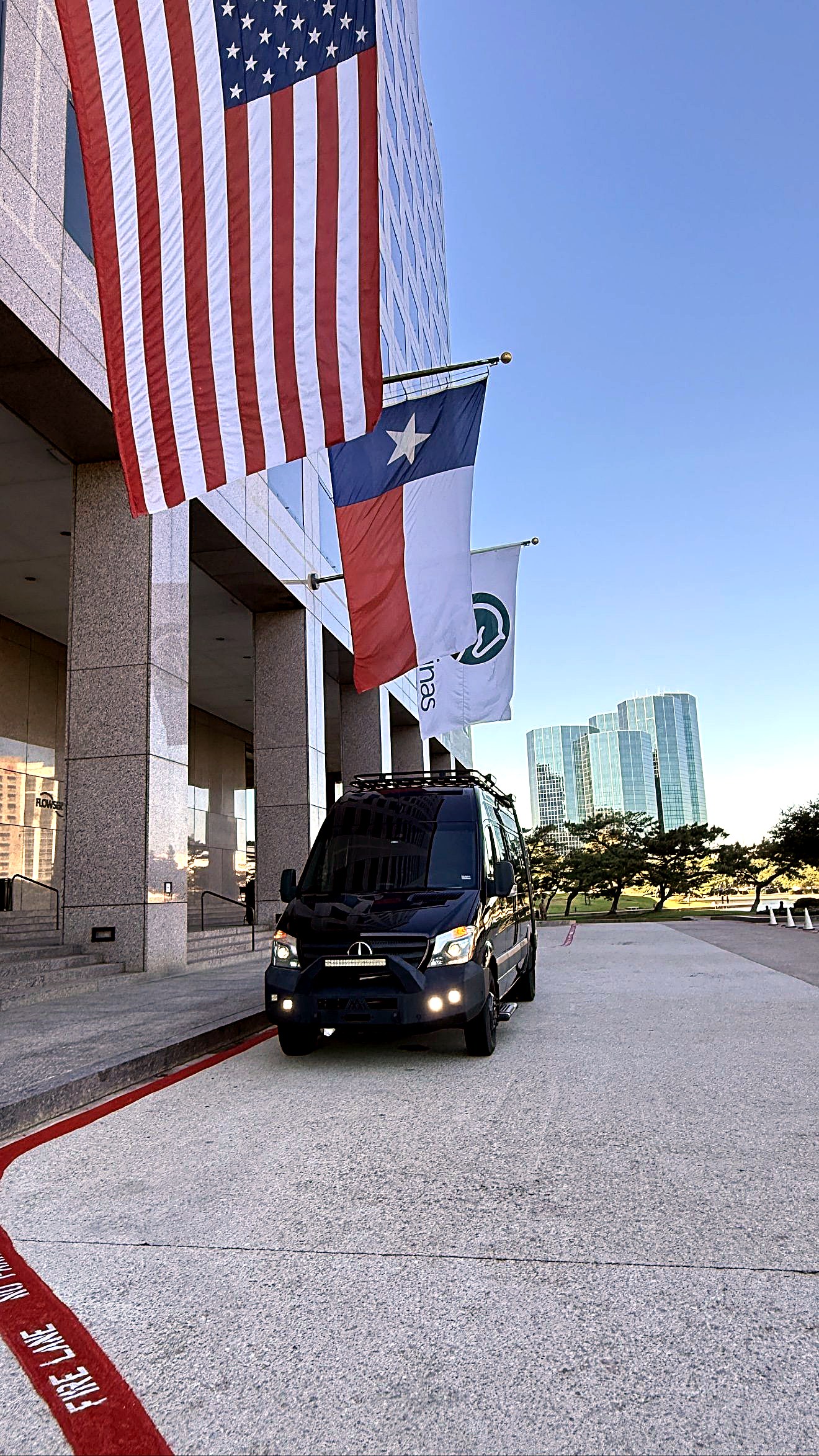 A black ExecSprinters Sprinter arriving at a venue entrance beneath the American and Texas flags