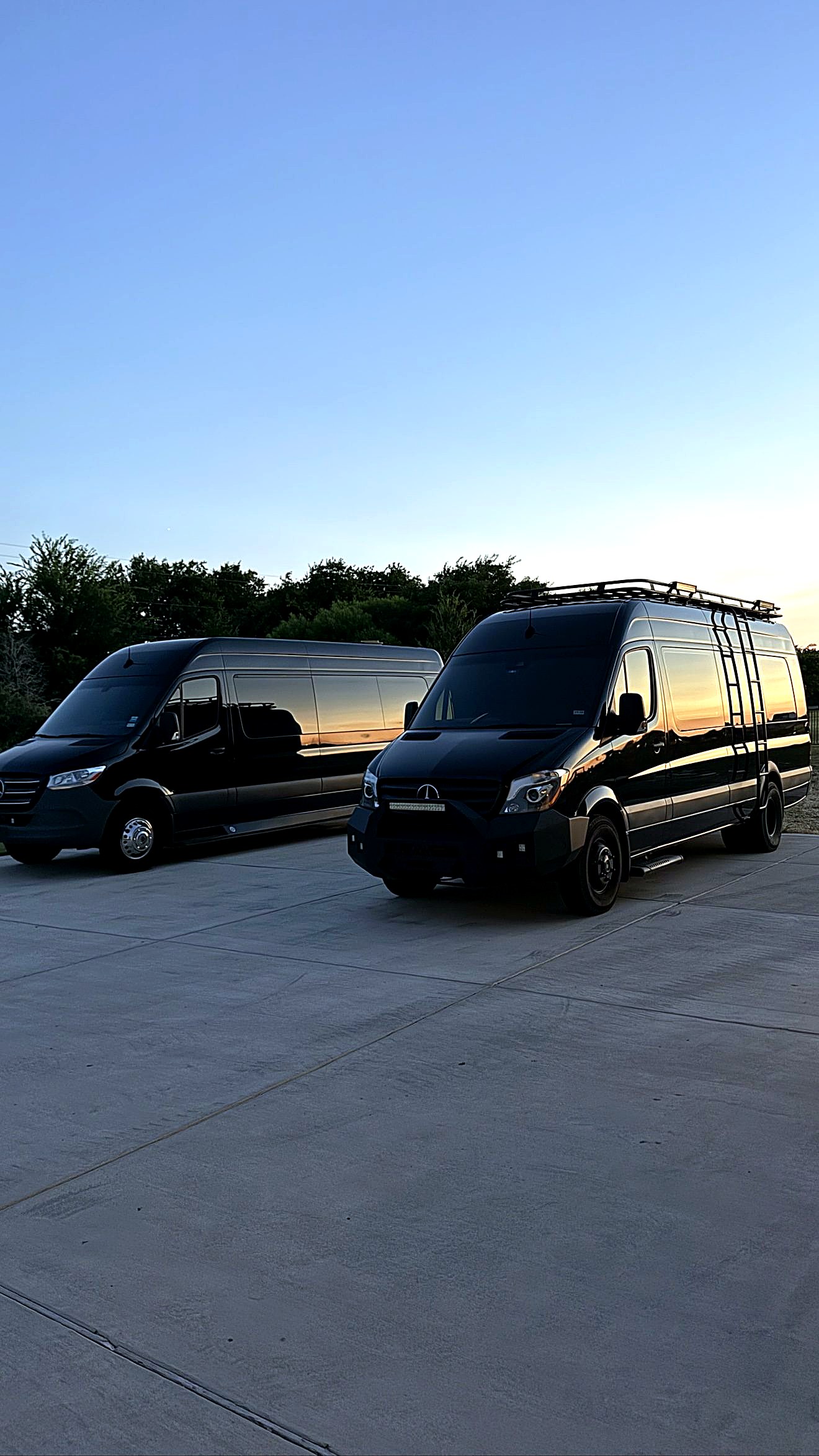 Two black ExecSprinters Mercedes-Benz Sprinters parked side by side at dusk